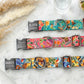 Three colorful dog collars with engraved nameplates on a marble surface.