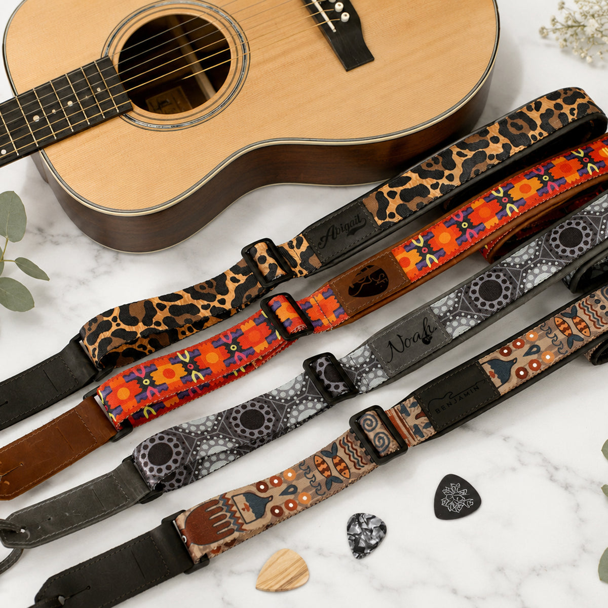 Guitar straps with various patterns on a marble surface with a guitar.