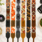 Collection of patterned camera straps on a marble surface with camera lenses.