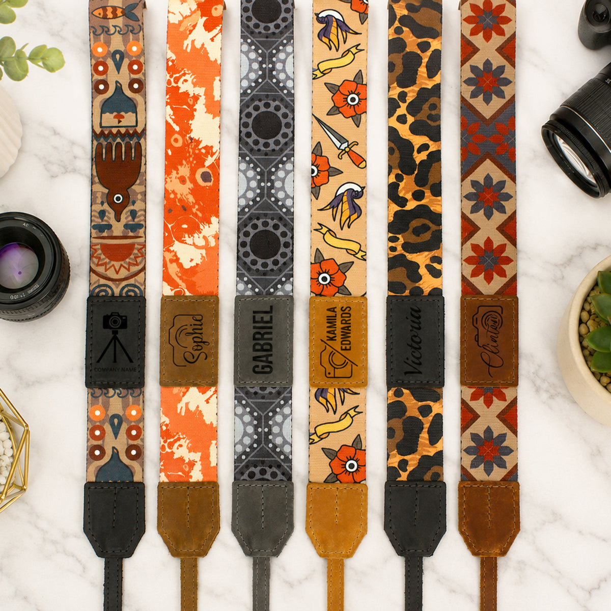 Collection of patterned camera straps on a marble surface with camera lenses.