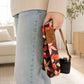 Person holding a floral-patterned camera strap with a brand tag in a living room setting.