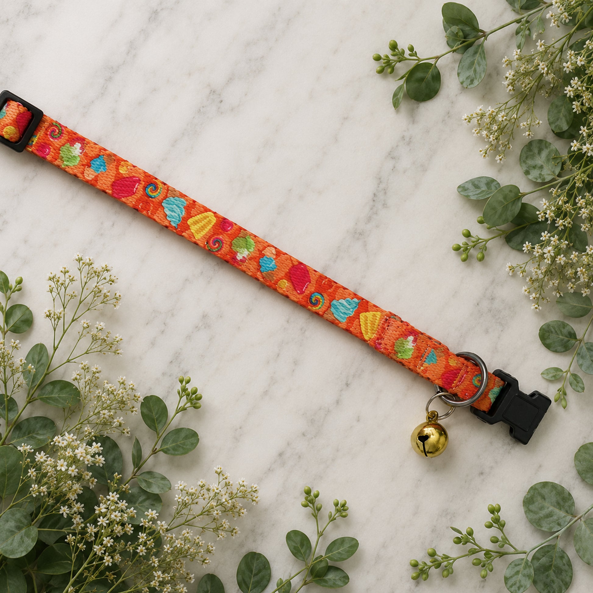 Colorful dog collar with a bell on a marble surface surrounded by greenery