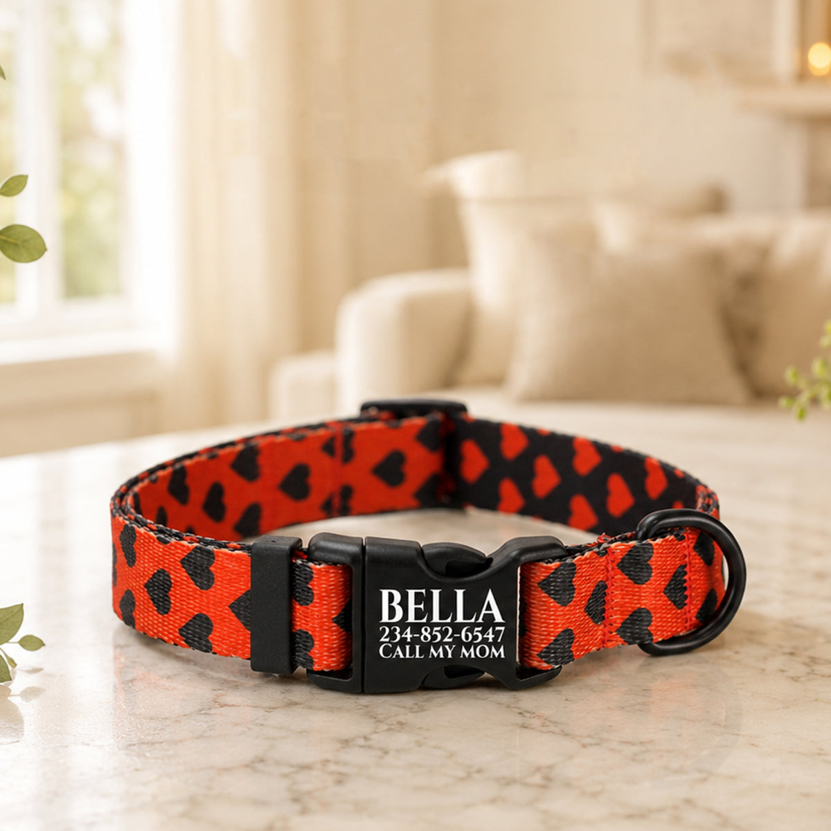 Red and black patterned dog collar with 'Bella' and contact information on a marble surface.