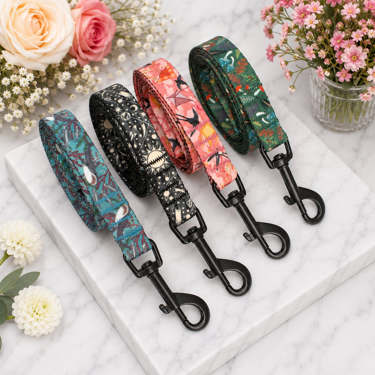 Four floral-patterned dog leashes on a marble surface with flowers around.