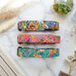 Three colorful dog collars on a marble surface with decorative elements.