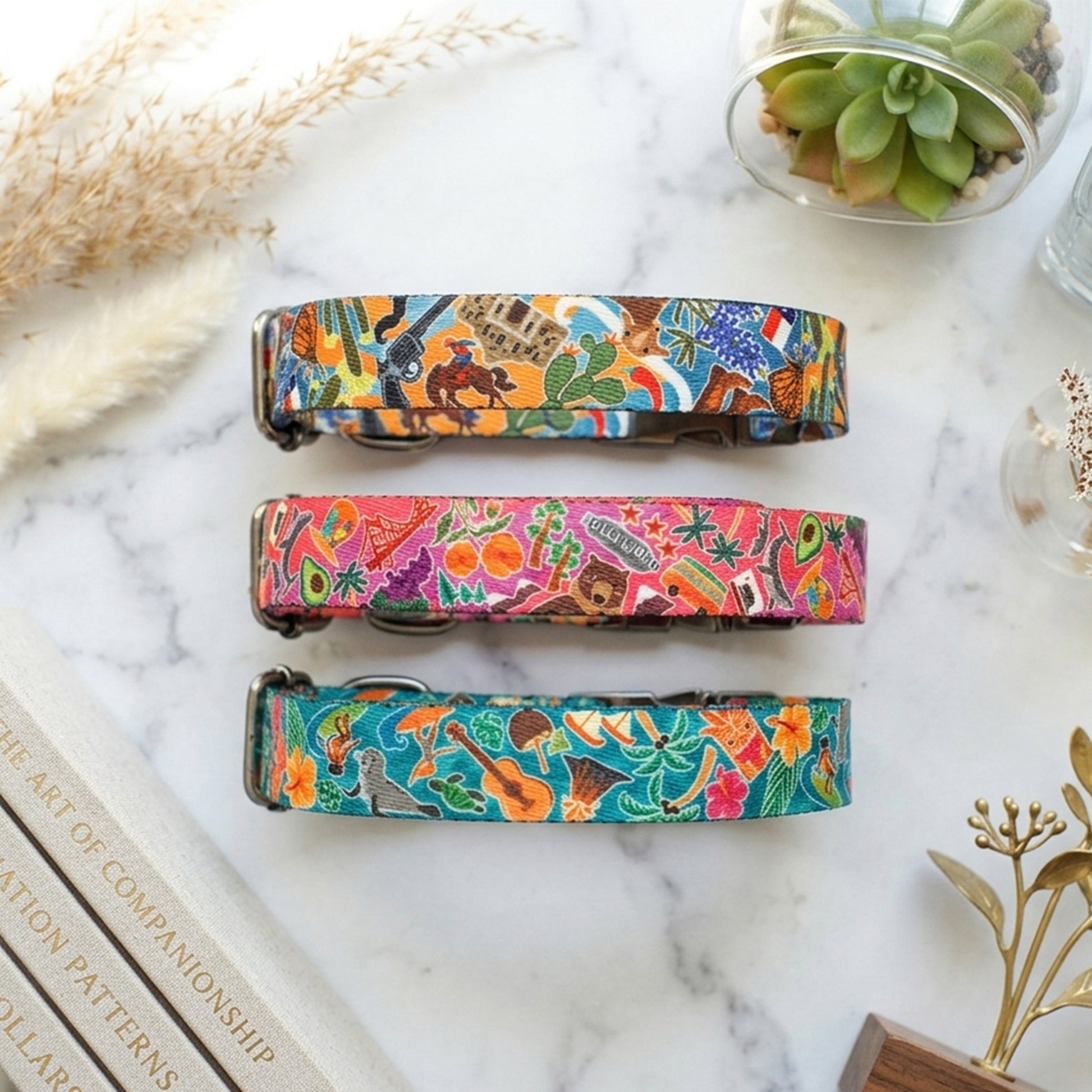 Three colorful dog collars on a marble surface with decorative elements.