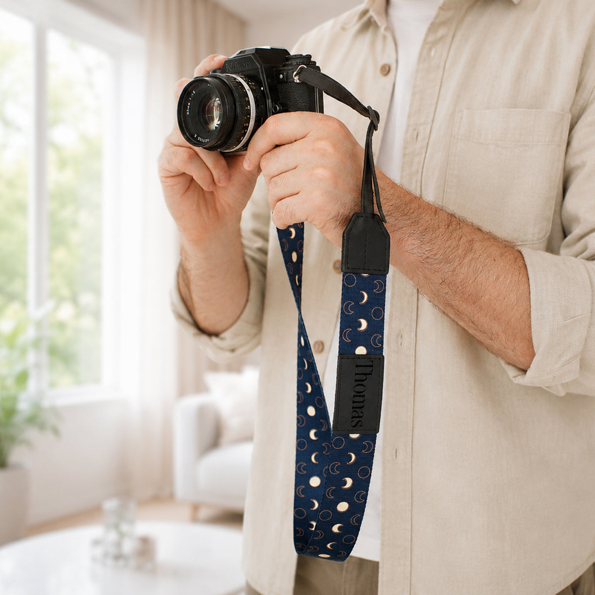 Person holding a camera with a blue polka dot strap in a living room setting