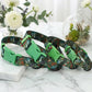 Two patterned dog collars with green buckles on a marble surface with decorative plants in the background.