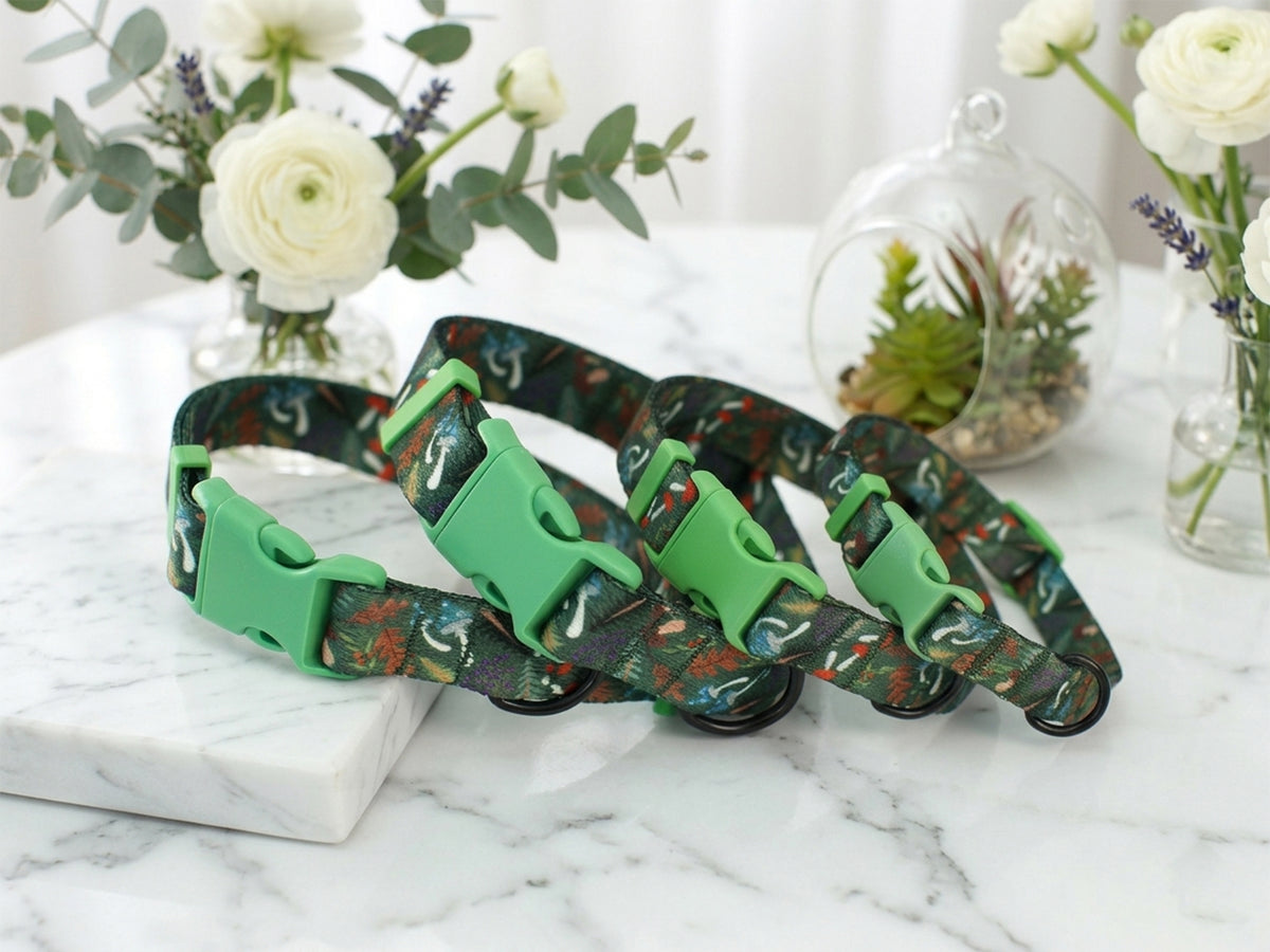 Two patterned dog collars with green buckles on a marble surface with decorative plants in the background.