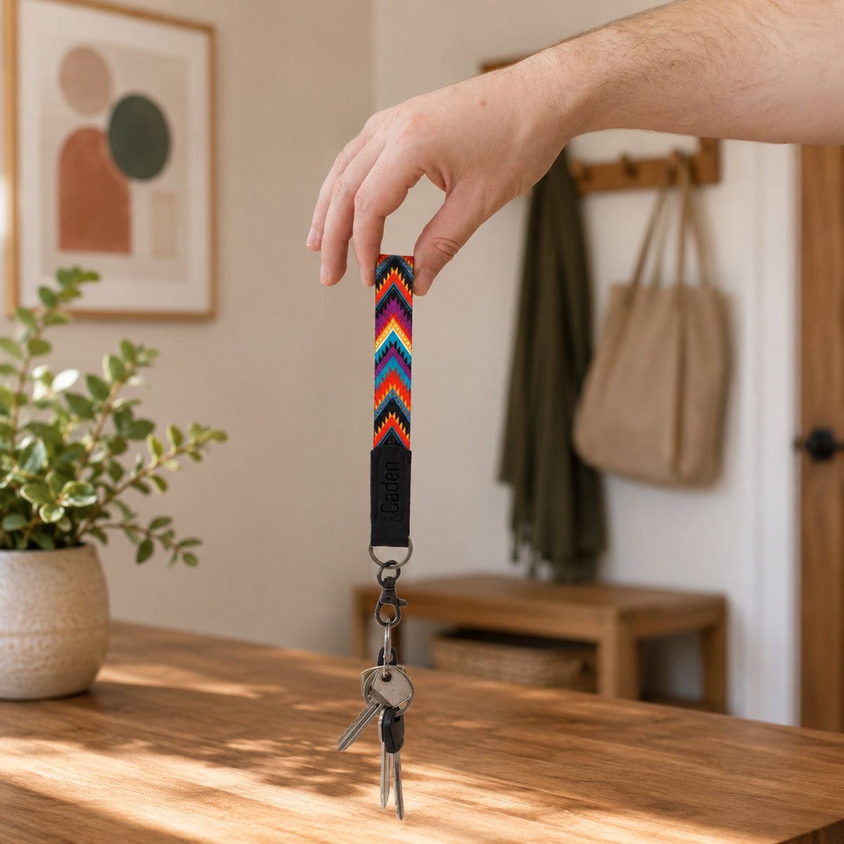 Hand holding a colorful keychain with keys on a wooden surface, with a blurred indoor background.