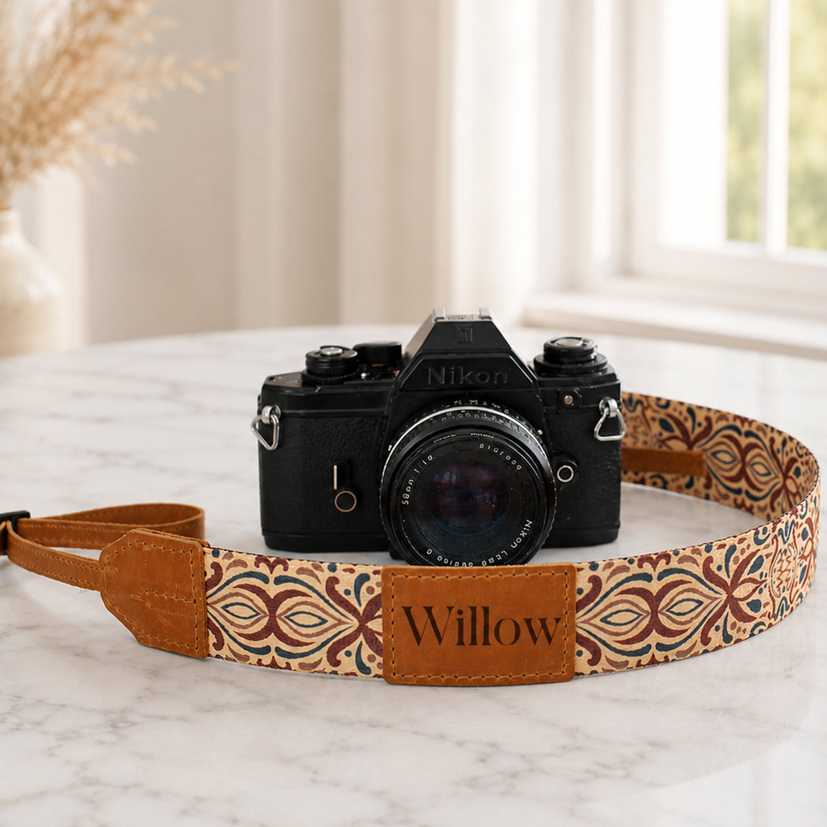 Camera with a patterned strap labeled 'Willow' on a marble surface.
