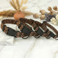 Leopard print dog collar with black hardware on a marble surface with decorative elements.