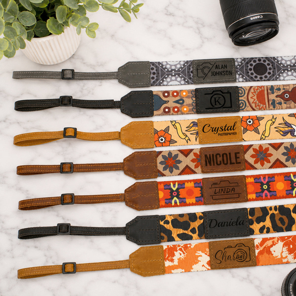 Collection of personalized camera straps with unique patterns and names on a marble surface.