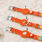 Three orange dog collars with colorful patterns on a marble surface
