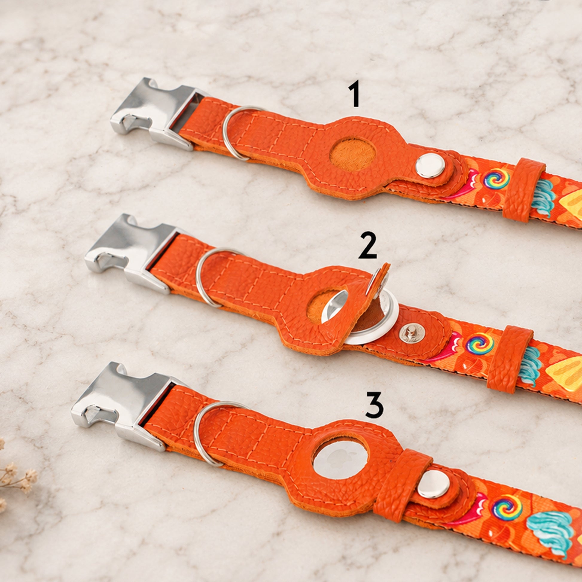 Three orange dog collars with colorful patterns on a marble surface