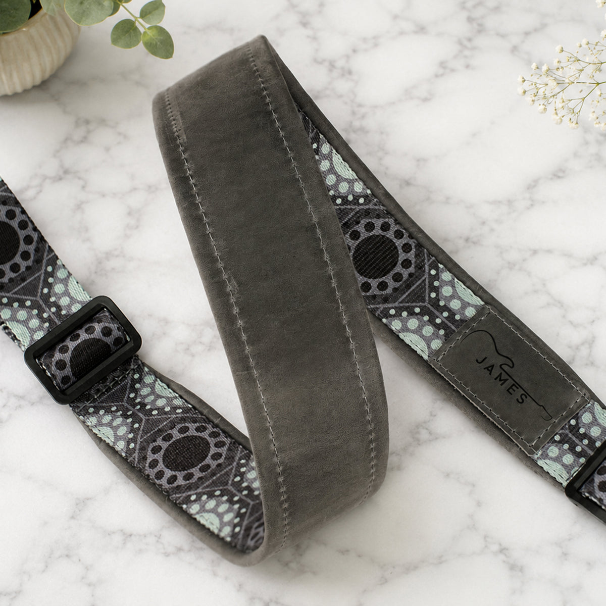 Gray guitar strap with patterned ends on a marble surface