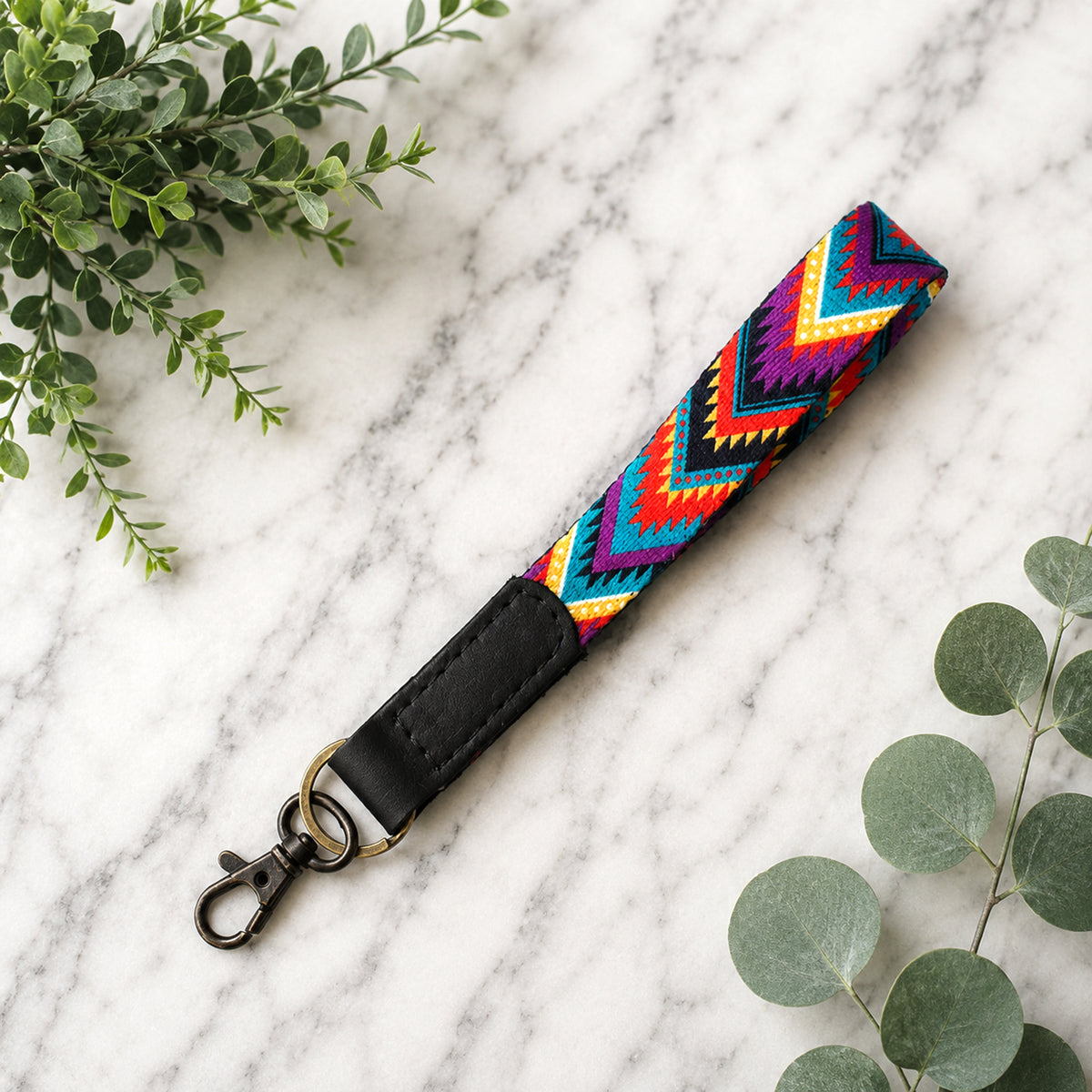 Colorful zigzag patterned strap with black end piece on a marble surface with green leaves.