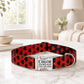 Red and black patterned dog collar with a silver buckle and engraved name and phone number on a marble surface.