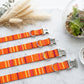 Set of orange striped dog collars with engraved names on a marble surface.