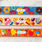 Three colorful belt straps with donut, cake, and candy patterns on a marble surface.
