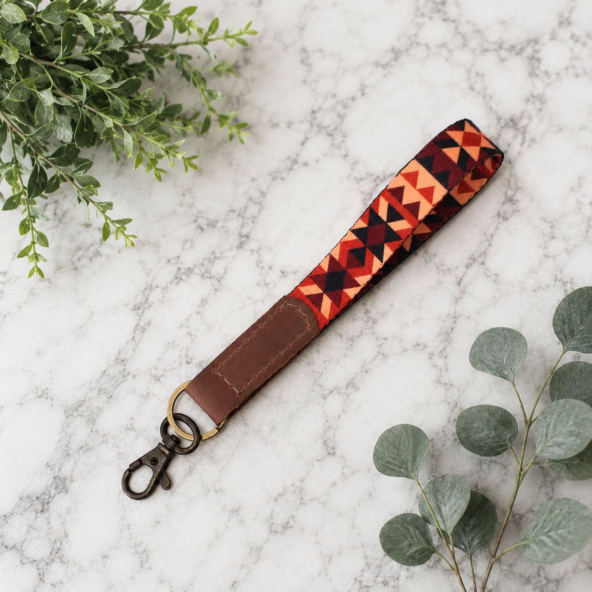 Patterned strap with brown leather end on a marble surface with green leaves.