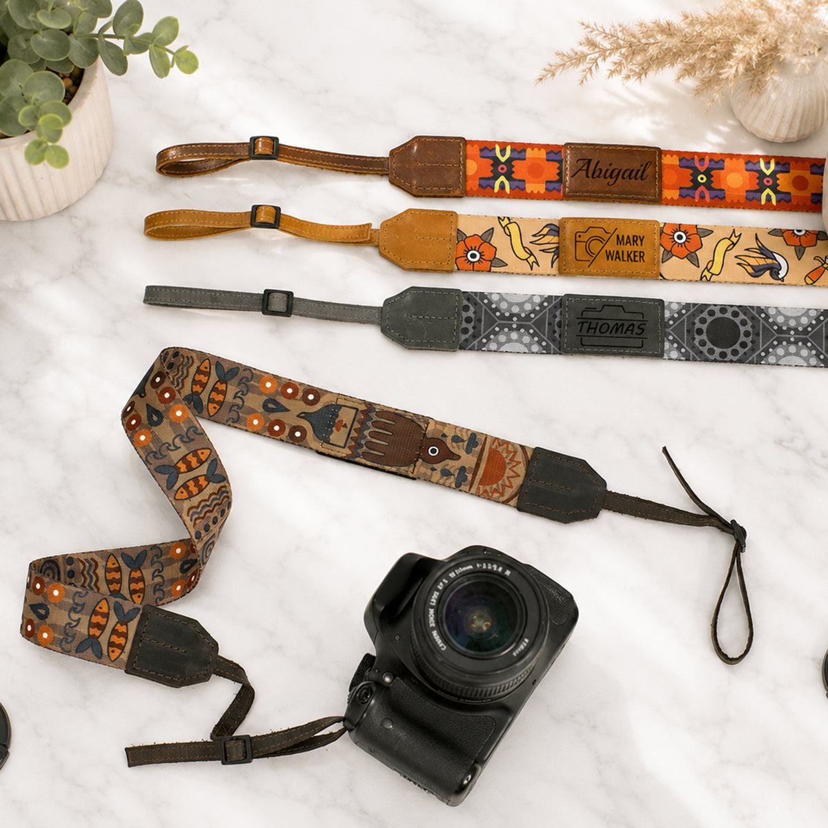 Camera with decorative camera strap on a light surface with plants