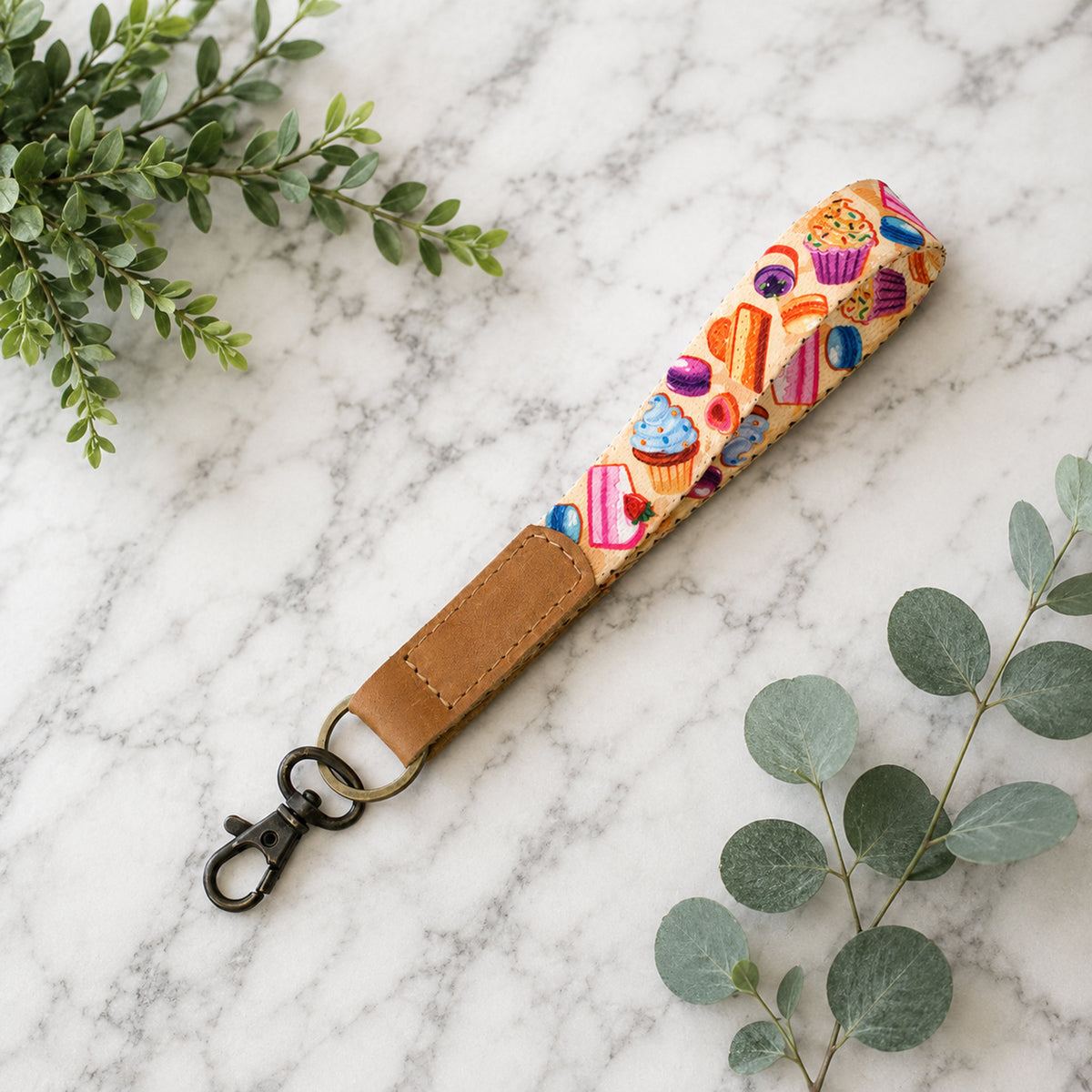 Colorful keychain strap with cupcake design on a marble surface with green leaves.