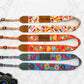 Four colorful camera straps with different patterns and names on a textured white background.