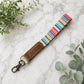 Colorful striped keychain with brown leather end on marble surface with green leaves