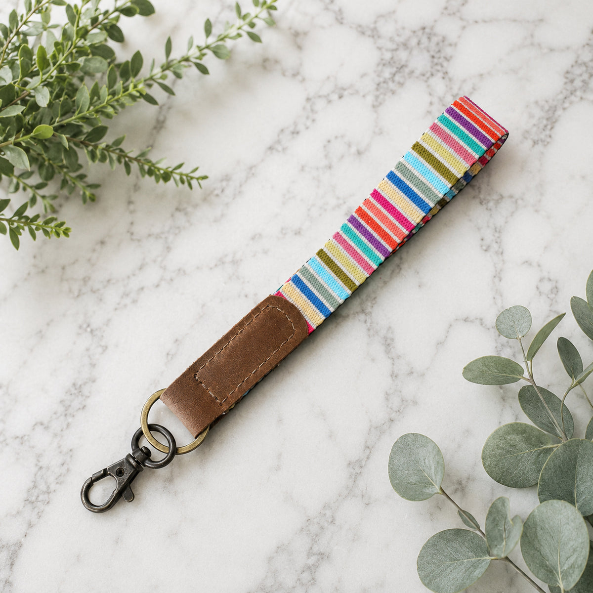 Colorful striped keychain with brown leather end on marble surface with green leaves