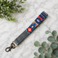 Colorful patterned keychain with gray strap on a marble surface with green leaves.