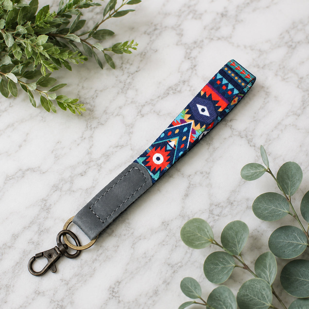 Colorful patterned keychain with gray strap on a marble surface with green leaves.