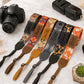 Collection of colorful camera straps with various patterns on a light surface, alongside a Canon camera and flash.