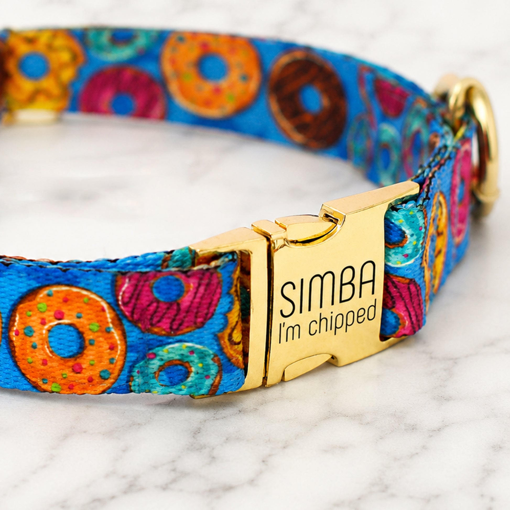 Colorful dog collar with gold buckle and 'Simba I'm chipped' tag on a marble background