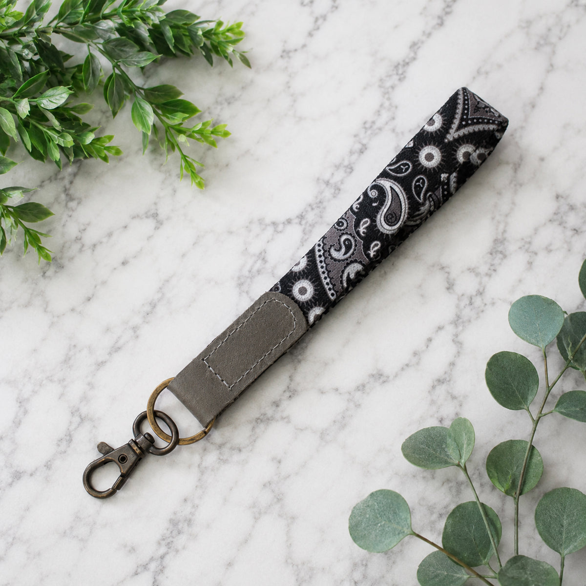 Keychain strap with paisley pattern on a marble surface with green leaves