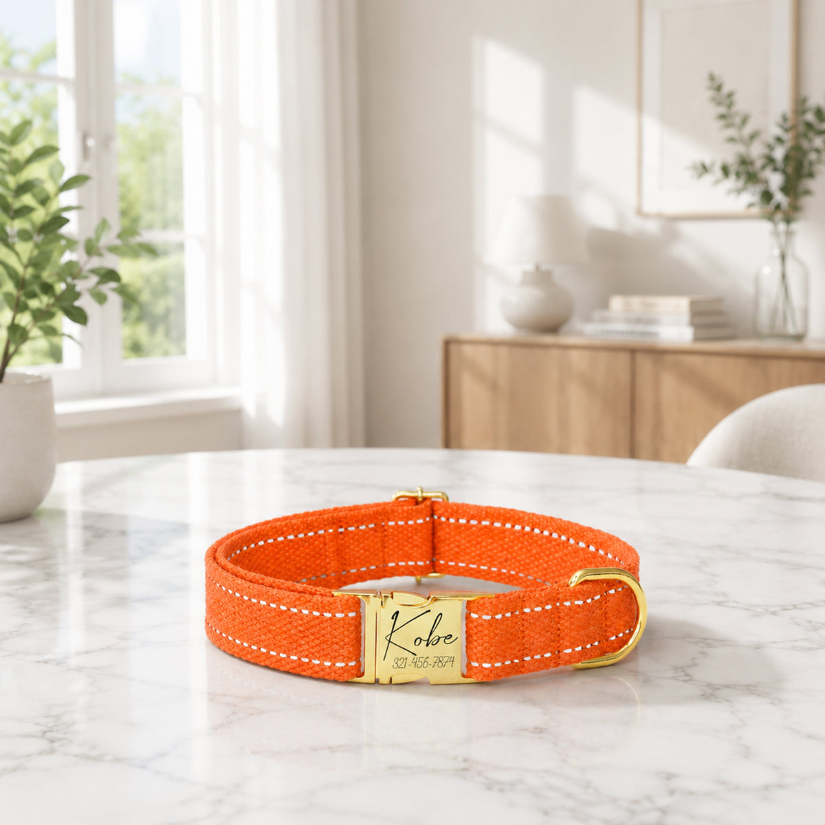 Orange dog collar with a gold tag on a marble surface in a bright room.