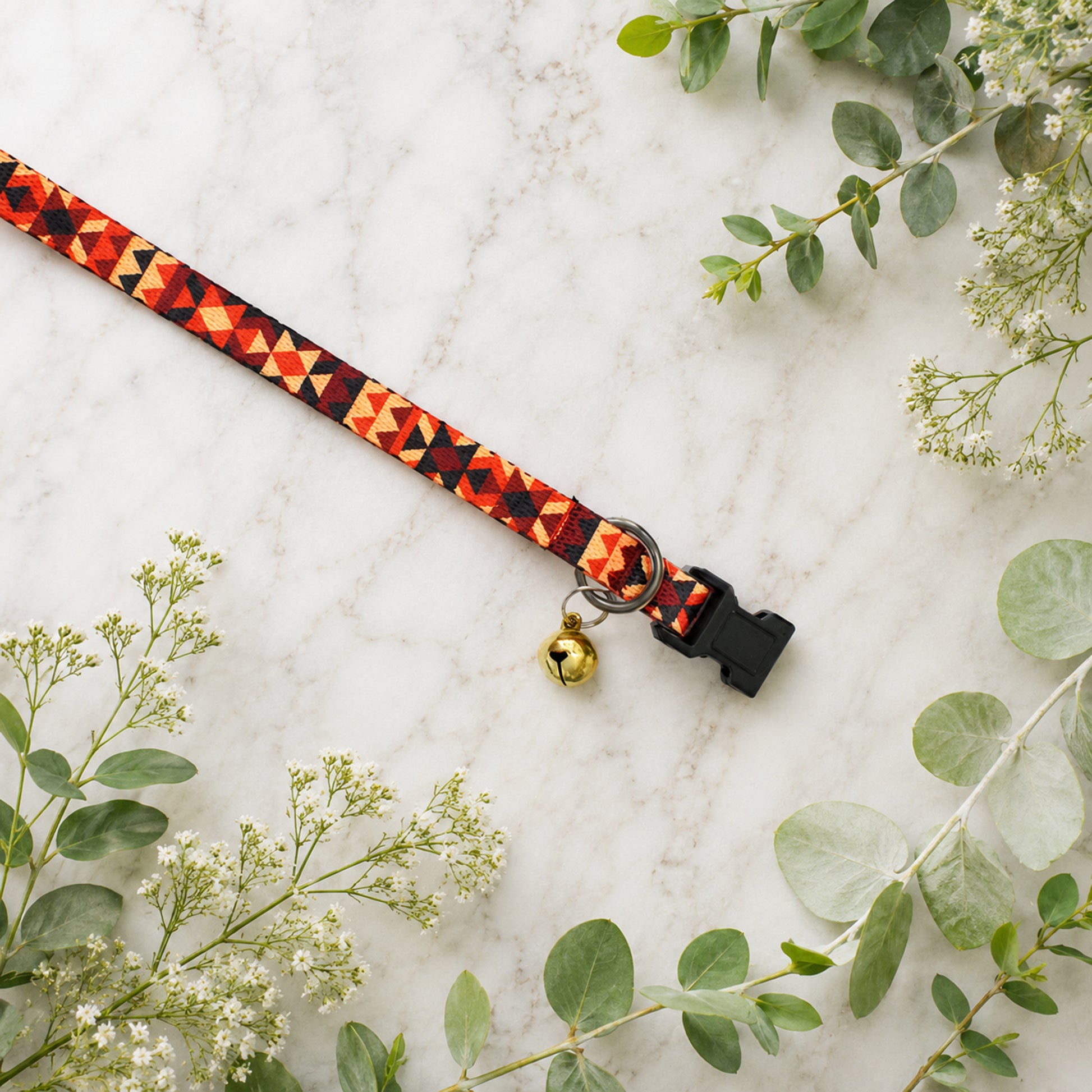 Decorative dog collar with geometric pattern and bell on a marble surface with greenery