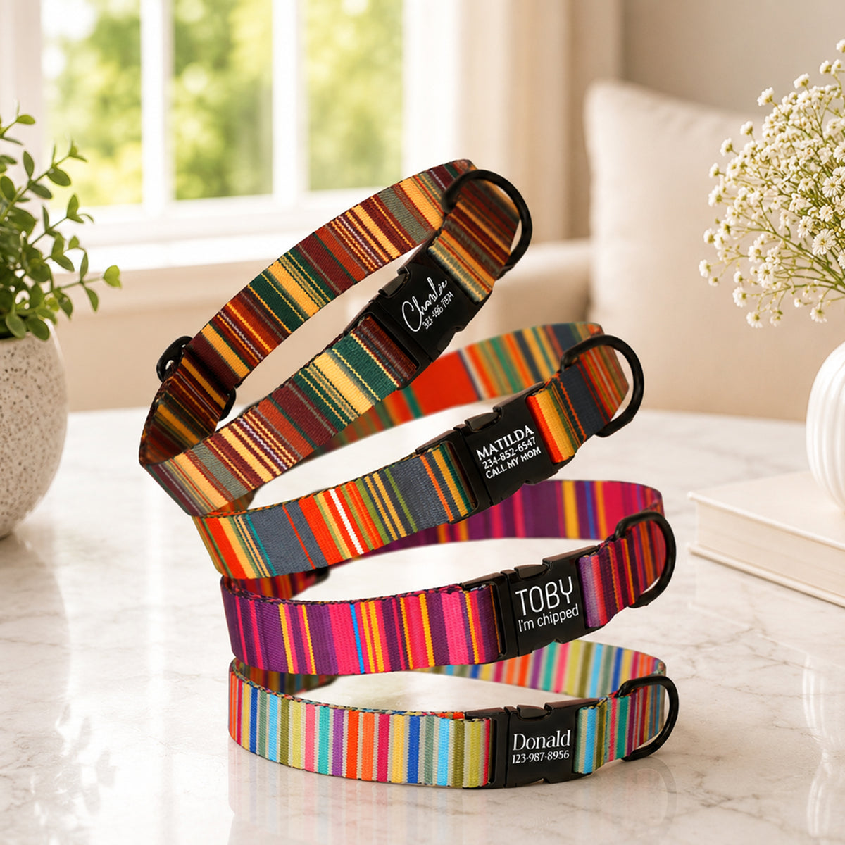 Set of colorful striped dog collars with engraved names on a marble surface.