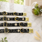 Four black dog collars with gold buckles and engraved names on a marble surface.
