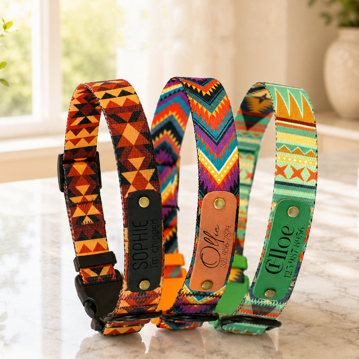 Three colorful dog collars with geometric patterns on a marble surface.