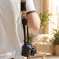 Person holding a camera with a colorful strap in an outdoor setting