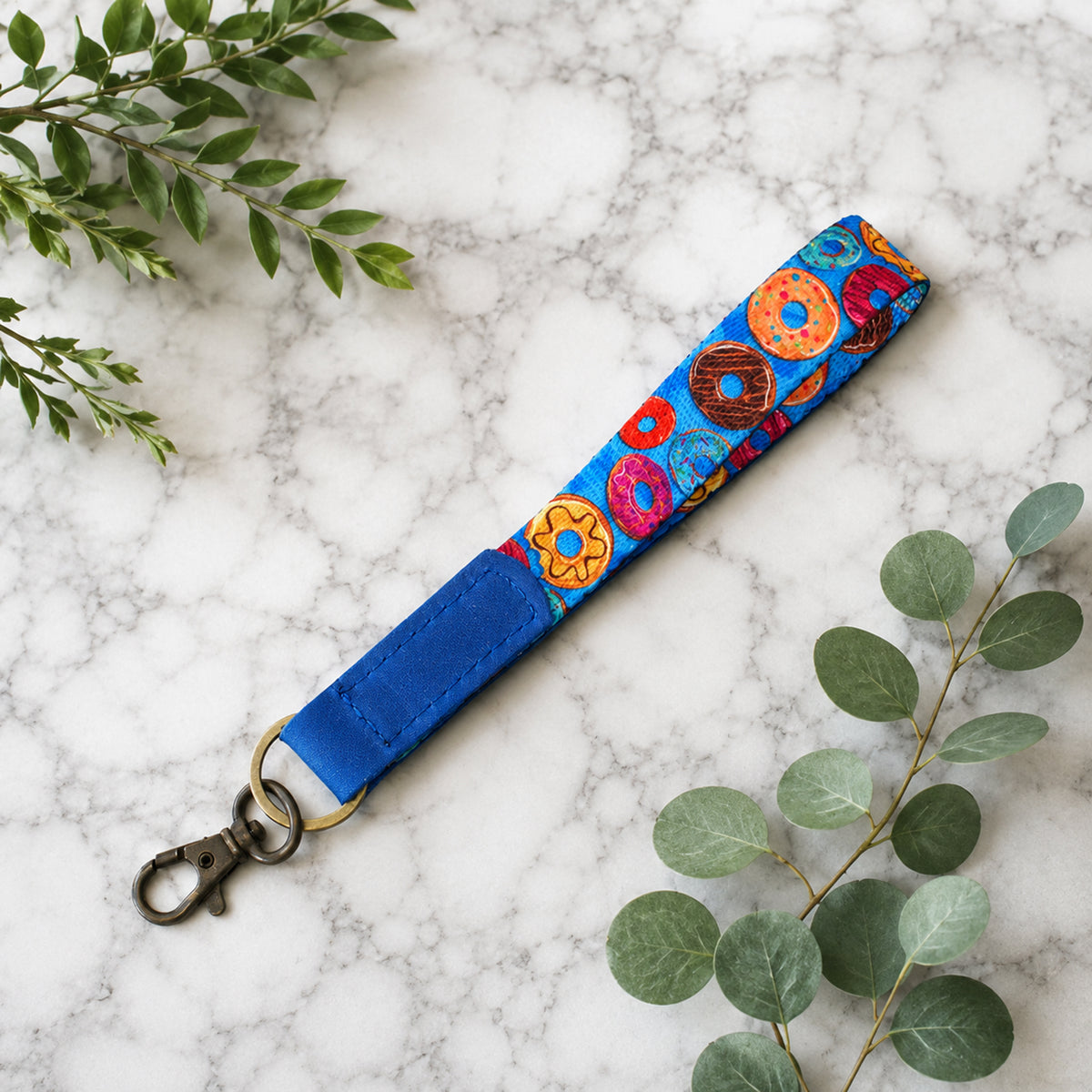 Colorful donut-patterned strap with blue end on a marble surface with green leaves.
