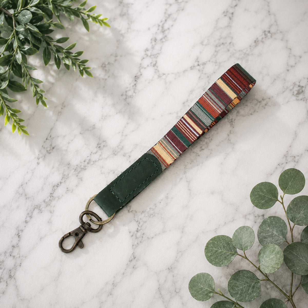Colorful striped keychain on a marble surface with green leaves