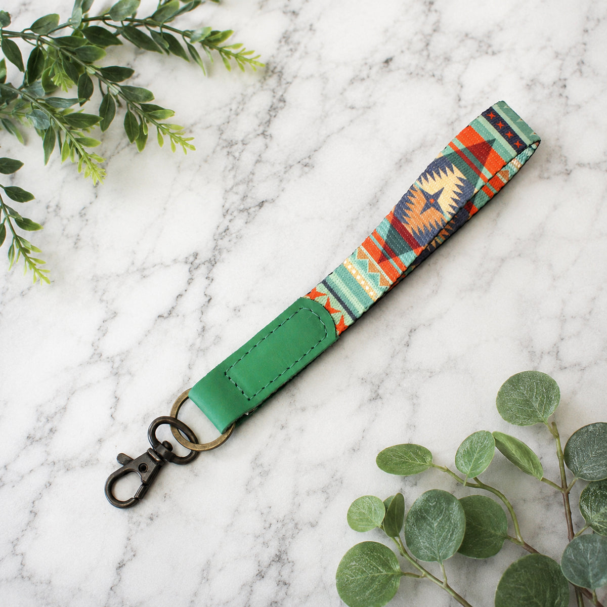 Colorful patterned strap with green accents on a marble surface with green leaves.