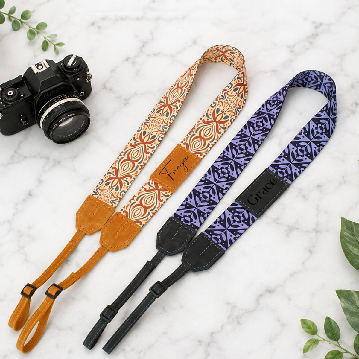Two camera straps with decorative patterns on a marble surface with a camera.