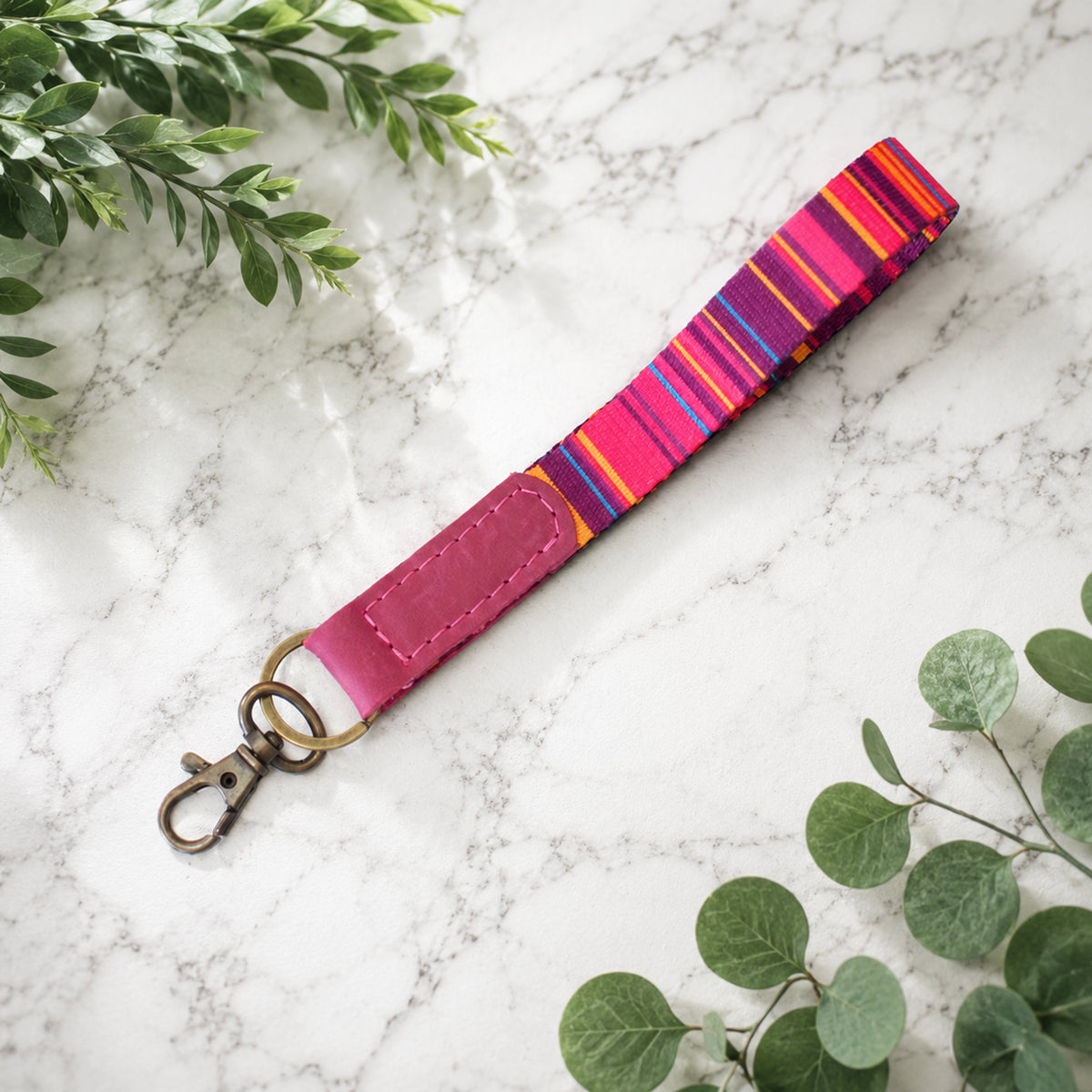Colorful striped keychain on a marble surface with green leaves