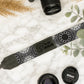 Camera strap with personalized engraving on a marble surface with camera lenses and leaves.