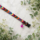 Colorful braided dog collar with a bell on a marble surface surrounded by greenery