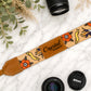 Camera strap with 'Crystal Photographer' leather patch, surrounded by Nikon lenses and greenery on a white marble surface.