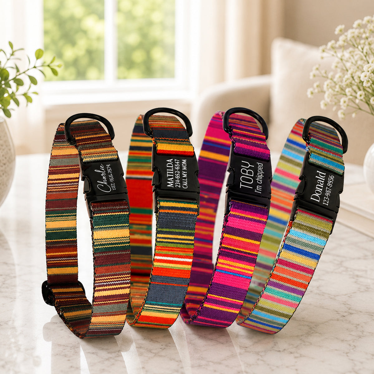 Four colorful striped dog collars with personalized names on a marble surface.